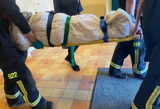 Personer från räddningstjänst bär en bår med en person insvept i täcke.